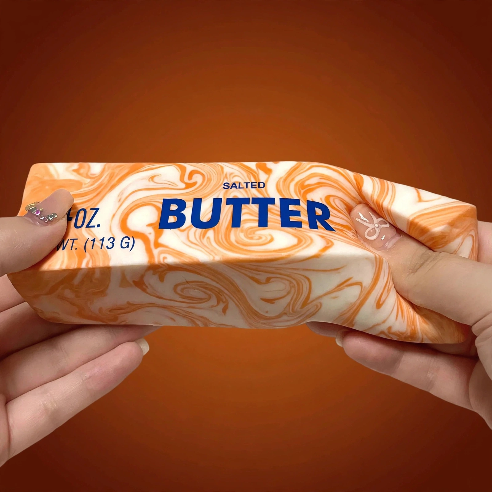 Hands squeezing the Orange marble butter squishy 4oz soft foam