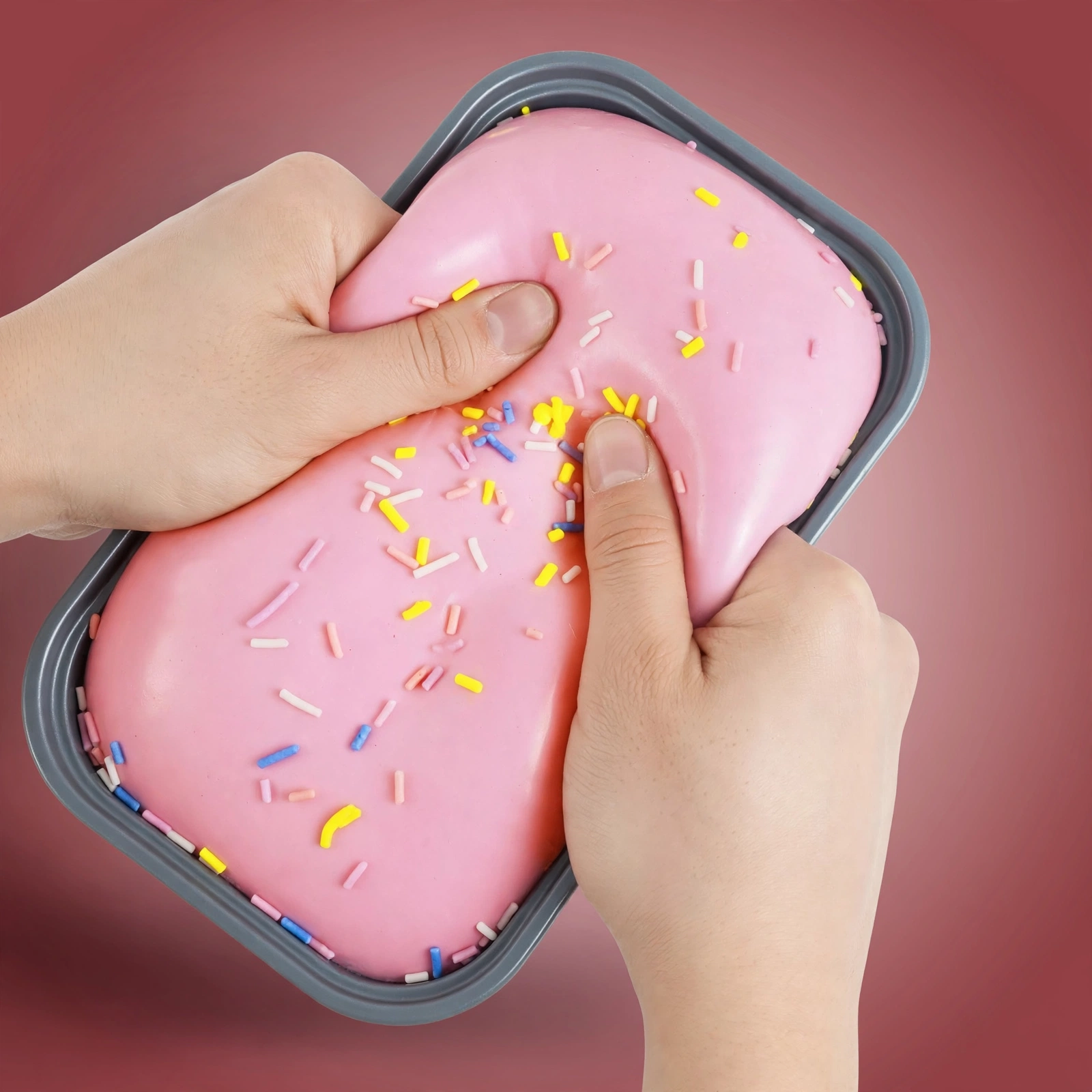 Hands squeezing the strawberry cake squishy in its tray